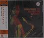 Text: "AFRICA/BRASS THE JOHN COLTRANE QUARTET". Japanische Schriftzeichen links. Jazzmusiker mit Saxophon, dunkler Hintergrund.