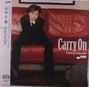 Text: „Carry On“, „Chihiro Yamanaka“. Eine Person sitzt in Anzug auf einem roten Sofa.