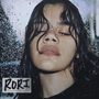 Text: "RORI". Eine Person mit nassen Haaren und geschlossenen Augen steht im Regen oder hinter einer regennassen Scheibe.