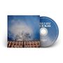 "LOVE IS BLISS" in Großbuchstaben auf einer CD. Ein Baum vor einem Gebäude und blauer Himmel im Hintergrund.