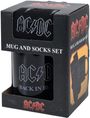 „AC/DC MUG AND SOCKS SET“. Schwarze Tasse mit „AC/DC BACK IN BLACK“-Aufdruck in einem schwarzen Karton mit rotem „AC/DC“-Logo.
