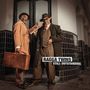 Text: "Ragga Twins Still Outstanding". Zwei stilvoll gekleidete Männer, einer mit Hut und Koffer, posieren selbstbewusst.