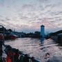 Ein ruhiger Hafen bei Sonnenuntergang, rote Boote, ein weißer Turm, und reflektierendes Wasser mit wolkigem Himmel.
