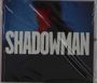Text: „SHADOWMAN“. Unscharfe Silhouette eines Mannes vor blau-rotem Hintergrund.