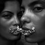 Zwei Gesichter nahe beieinander, verbunden durch eine kunstvolle, metallische Kette über den Lippen.