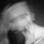 Verschwommenes, schwarz-weißes Porträt einer Person mit Hand am Kinn, in Bewegung.