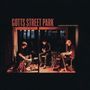 Text: "GOTTS STREET PARK" und "SOMEWHERE BETWEEN". Drei Personen spielen Instrumente in einem gemütlich beleuchteten Raum.