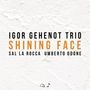 IGOR GEHENOT TRIO, SHINING FACE, SAL LA ROCCA, UMBERTO ODONE; schwarzer und oranger Text auf strukturiertem weißen Hintergrund.