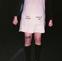 Text auf einem Kleid: „SELF HATRED“ und „MASSIVE EGO“. Jemand steht mit geballten Fäusten, trägt Stiefel und hat ein Bein-Tattoo.