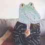 Eine Person hält eine gezeichnete Krokodilmaske vor das Gesicht, sitzend auf einem Sofa.