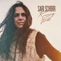 "SARI SCHORR Running Wild" in eleganter Schrift. Eine Frau mit langen Haaren und einer Fellweste blickt ruhig in die Kamera.