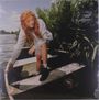 Ein Mädchen mit langen, lockigen Haaren sitzt in einem Boot und blickt nach unten; im Hintergrund Wasser und Pflanzen.