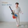 „Vesper, Sean Shibe.“ Ein Mann in Weiß hält eine bunt gestaltete Gitarre, neben ihm eine weiße Substanz am Boden.