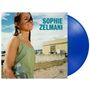 „Sophie Zelmani“ in türkisfarbener Schrift. Eine lächelnde Frau im Sommerkleid hält eine Wasserflasche; daneben eine blaue Schallplatte.