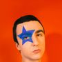 Ein Mann vor orangenem Hintergrund, Gesicht zum Betrachter. Ein blauer Stern ist um sein rechtes Auge gemalt.