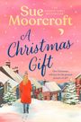 „Sue Moorcroft, A Christmas Gift. This Christmas, will love be the greatest present of all?“ zeigt eine Frau im Winterdorf.