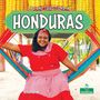 „Life and Traditions in Honduras“. Frau in rotem Kleid sitzt auf bunter Hängematte, lächelt, Hintergrund voller Maiskolben.