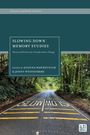 Text oben: "CRITICAL MEMORY STUDIES". Haupttext: "SLOWING DOWN MEMORY STUDIES". Straße im Wald mit "SLOW DOWN".