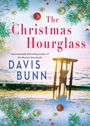 "The Christmas Hourglass" von Davis Bunn. Sanduhr am Meer bei Sonnenuntergang, umgeben von Tannenzweigen und Kugeln.