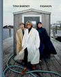 Text: "TINA BARNEY FASHION". Drei Männer in langen Mänteln stehen auf einem Dock vor einem kleinen Holzgebäude, mit Wasser im Hintergrund.