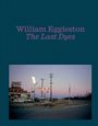 "William Eggleston The Last Dyes". Eine Tankstelle bei Dämmerung, mit Neonlichtern und Stromleitungen am Straßenrand.