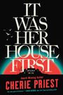 "IT WAS HER HOUSE FIRST" in großer Schrift. Darunter "CHERIE PRIEST". Silhouette eines Hauses vor rotem und blauem Hintergrund.
