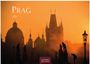 Prag 2027. Silhouetten von Türmen und Statuen bei Sonnenuntergang, mit einem orangefarbenen Himmel im Hintergrund.