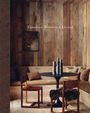 "Timeless Mountain Living" steht auf Holzwand. Gemütliche Ecke mit Holzwänden, Rundtisch, Stühlen, Kissen und rustikalem Dekor.