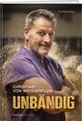 „Christian von Weissenfluh - Unbändig“ in weiß und gelb. Mann in lila Hemd, verschränkt die Arme, mit Sand umgeben.