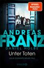 Titel: "Unter Toten" von Andreas Franz und Daniel Holbe. Ein offenes Garagentor zeigt Häuser in einer ruhigen Straße.
