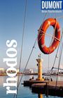 Text: "rhodos", "DUMONT Reise-Taschenbuch". Ein oranger Rettungsring hängt vor einem Hafen mit einer Säule und Skulptur im Hintergrund.