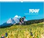 "TOUR Faszination Rennrad 2027". Ein Radfahrer auf einer Wiese, im Hintergrund Berge unter blauem Himmel.