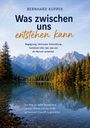 „Was zwischen uns entstehen kann“ von Bernhard Kuppek. See vor Berglandschaft, umgeben von Wäldern bei klarem Himmel.