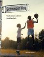 Straßenschild "Schwarzer Weg". Zwei Jugendliche spielen Basketball im Freien bei Sonnenuntergang.