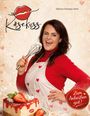 „Käsekuss“, „Zum Anbeißen gut!“. Frau mit Schneebesen und Sahnekuchen, trägt Herzschürze und lächelt.