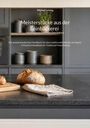 "Meisterstücke aus der Feinbäckerei" von Michael Leising. Ein Laib Brot liegt auf einem grauen Küchentresen.