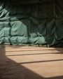 Grüne Plane, gespannt und gefaltet; Licht- und Schattenmuster auf hellem, kahlem Boden darunter.