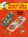 "Lucky Luke", "Die Grimm Brothers". Cowboy liegt in gläsernem Sarg, von Tieren umgeben. Links vier Figuren, typisch westlicher Stil.