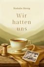 „Nathalie Hertig - Wir hatten uns“. Eine Tasse Kaffee, Garnrolle und altes Foto auf Holzuntergrund vor Berglandschaft.