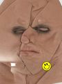 😊 Ein gelbes Smiley-Gesicht auf einer verzerrten, zusammengefalteten Gesichtsskulptur in Hautfarben mit geschlossenen Augen.