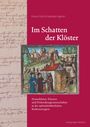 Titel: Im Schatten der Klöster. Illustration: Mönche und Gebäude in hügeliger Landschaft. Links Schriftrolle.