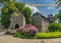 "Holger Klaes Bergisches Land 2027" steht zentral. Historische Gebäude, blühender Rhododendron und Kopfsteinpflaster.