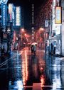 Regenbedeckte Straße, Neonlichter reflektieren auf dem Boden; „Junya Watanabe“. Menschen mit Regenschirmen.