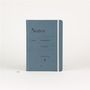 Auf einem blaugrauen Notizbuch steht: "Notes, Urtext, Notenbuch M, Music journal M, C. Henle Verlag". Weiße Gummibandbindung.