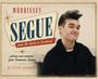 "MORRISSEY SEQUE", "from The Smiths to Suedehead". Mann mit hochtoupierten Haaren und schwarzem Pullover lächelt leicht.