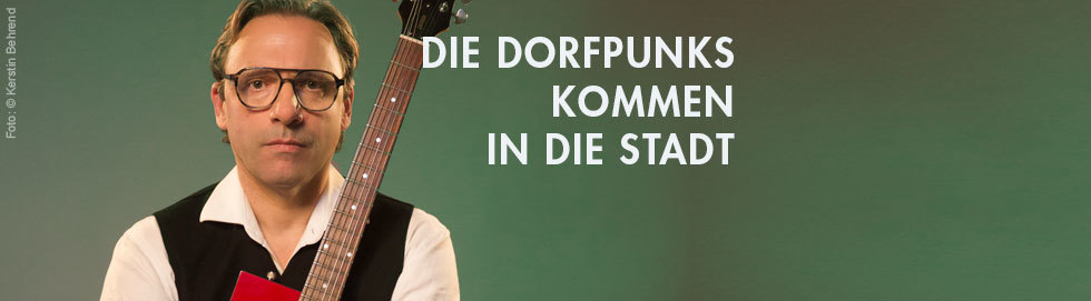 Rocko Schamoni mit Gitarra vor einem grünen Hintergrund